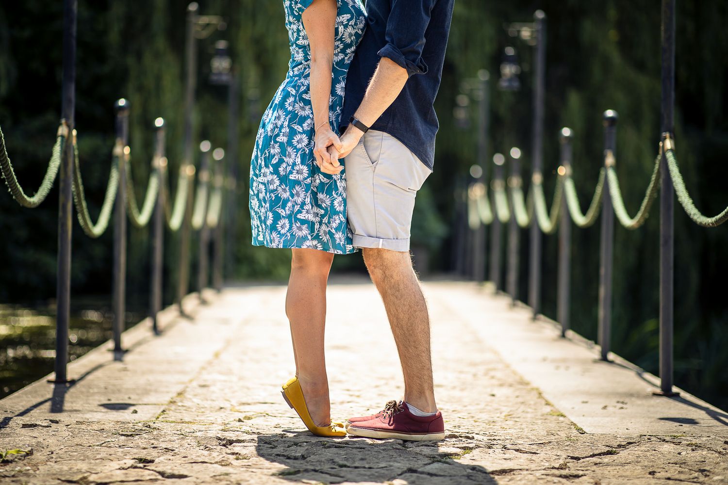 Close-up of feet in casual shoes and sandals standing together on a wooden bridge or walkway during a sunny day.
