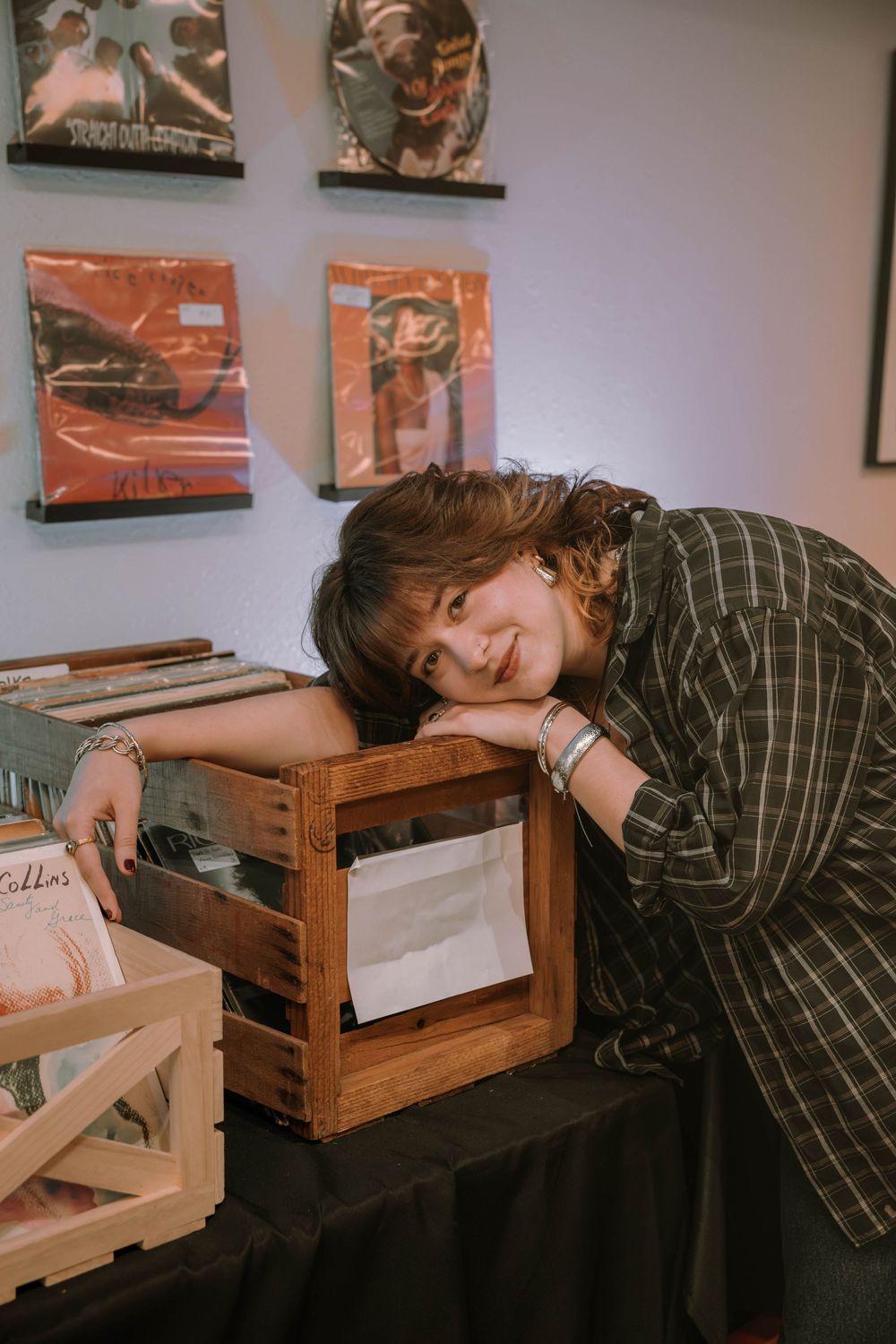 Three moody vintage-style photos show a person in a striped shirt resting their head on a wooden crate in an art gallery setting.