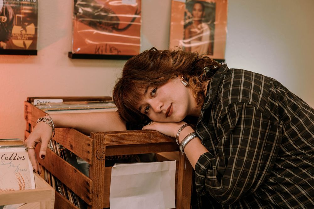 Someone in a black and white striped shirt rests their head on a wooden record crate in a vintage-toned setting.