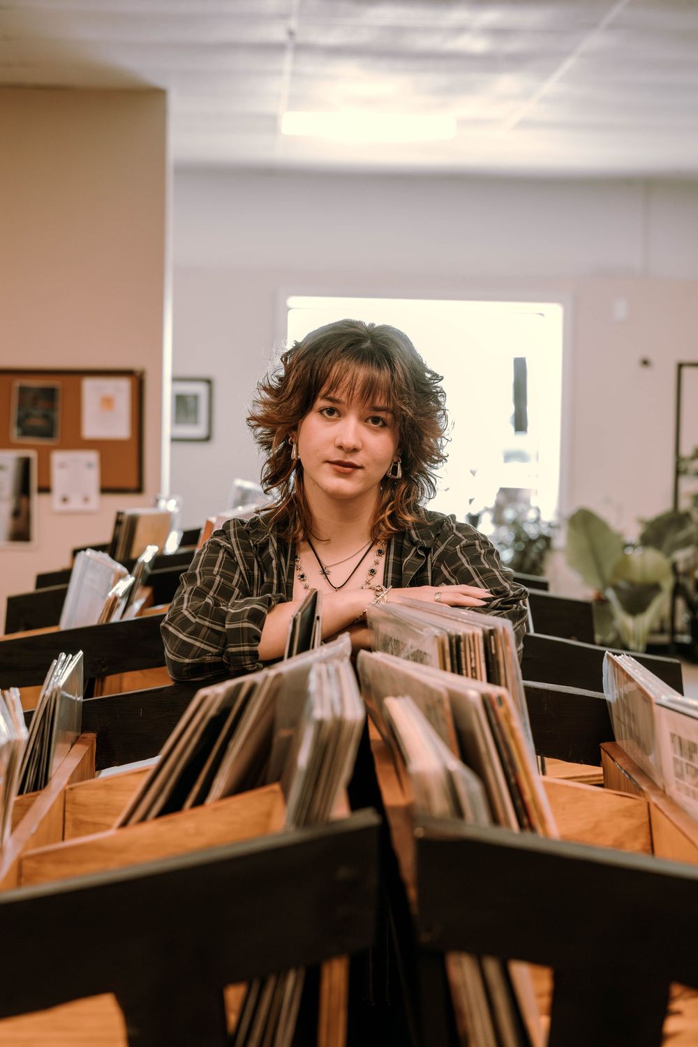 Someone peeks playfully over rows of vinyl records in a music store.