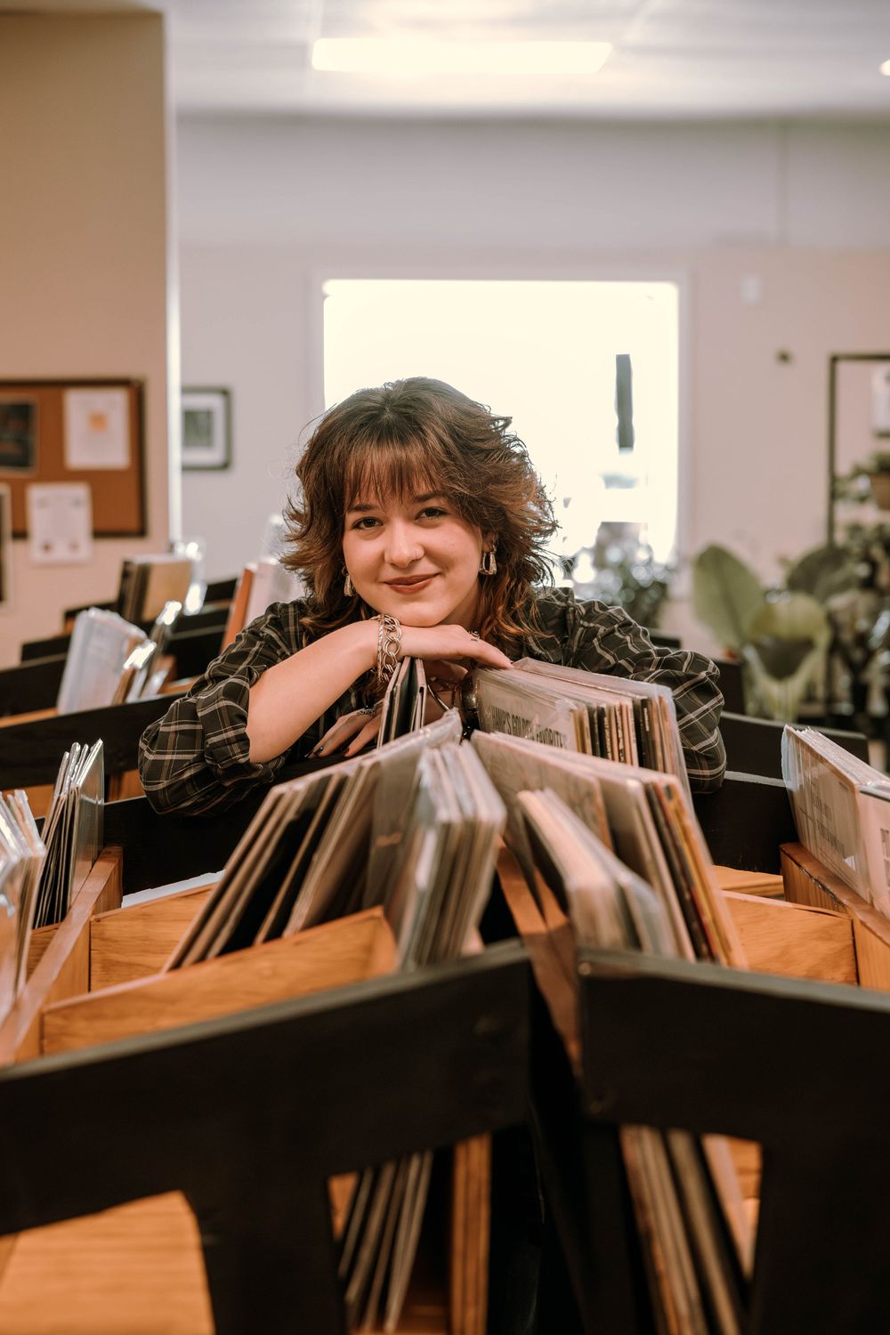 Someone browsing through vinyl records in a record store while leaning on the display case and smiling.