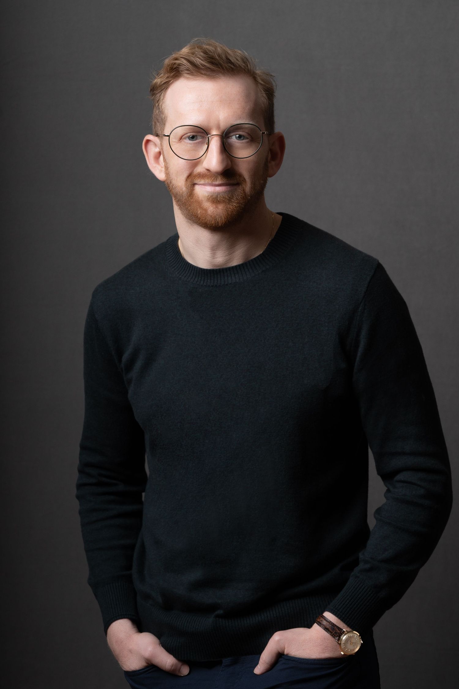 Professional portrait series of someone wearing black turtleneck and glasses against gray studio background.