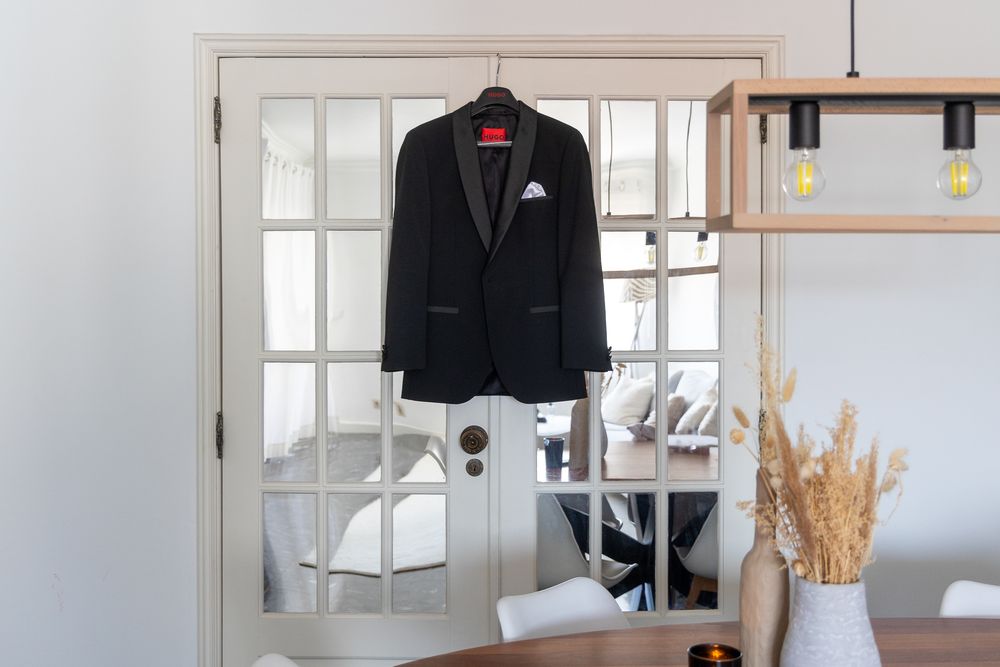 Black formal suit jacket hanging on wooden door with mirror reflection.