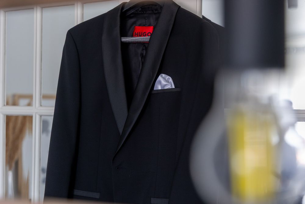 Close-up of black tuxedo jacket with pocket square hanging on display.