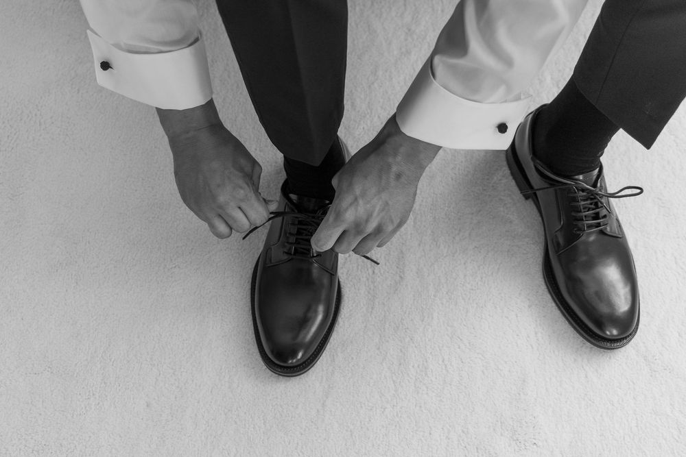 Close-up view of hands tying elegant black dress shoes on a white floor.