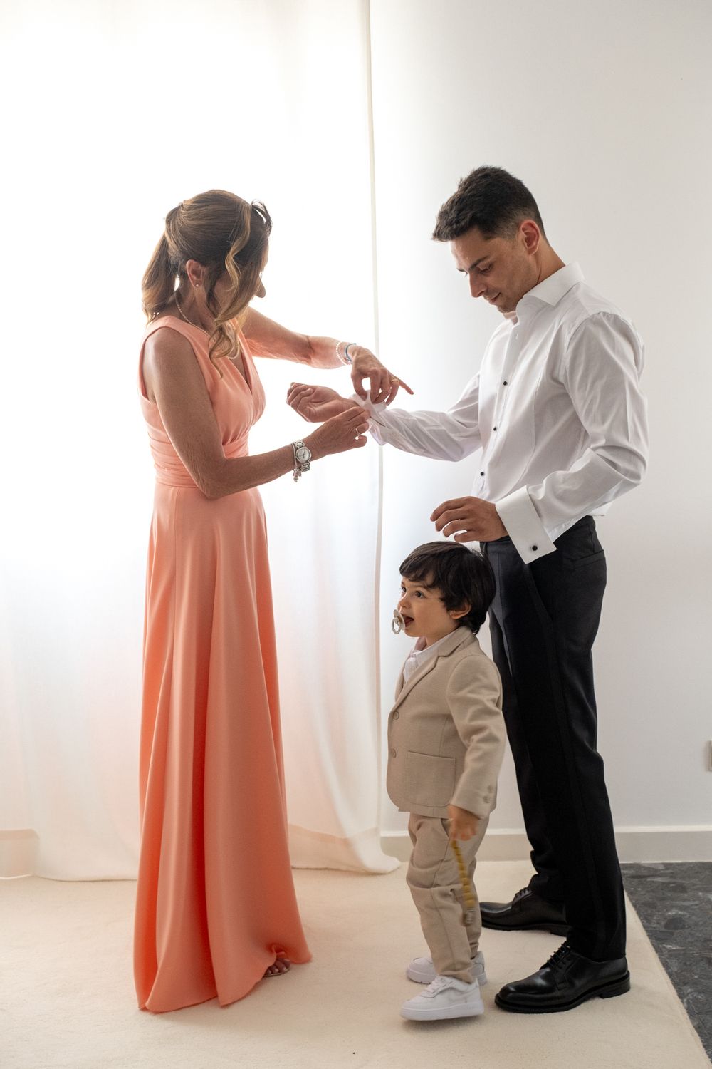 A touching family moment captured in formal wear with a small child in beige suit.