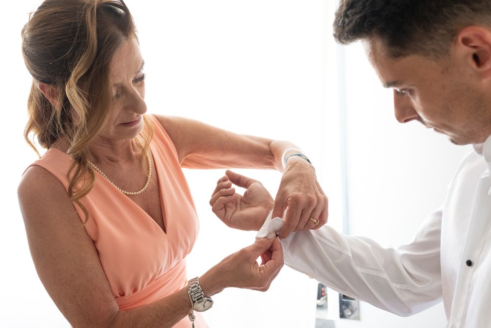 Close-up of hands adjusting cufflinks with person in coral dress assisting.