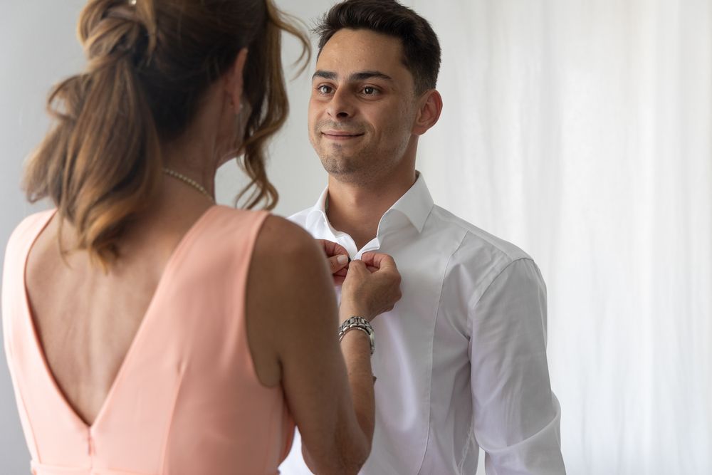 Intimate moment during formal dressing between two people in white and coral attire.