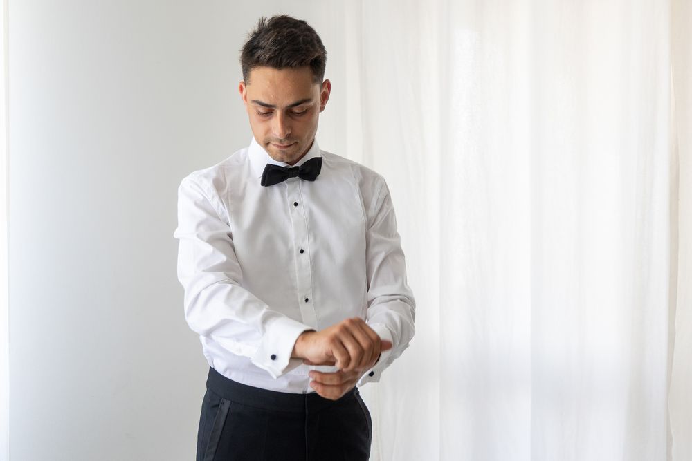 Person adjusting black bow tie while wearing white formal shirt.