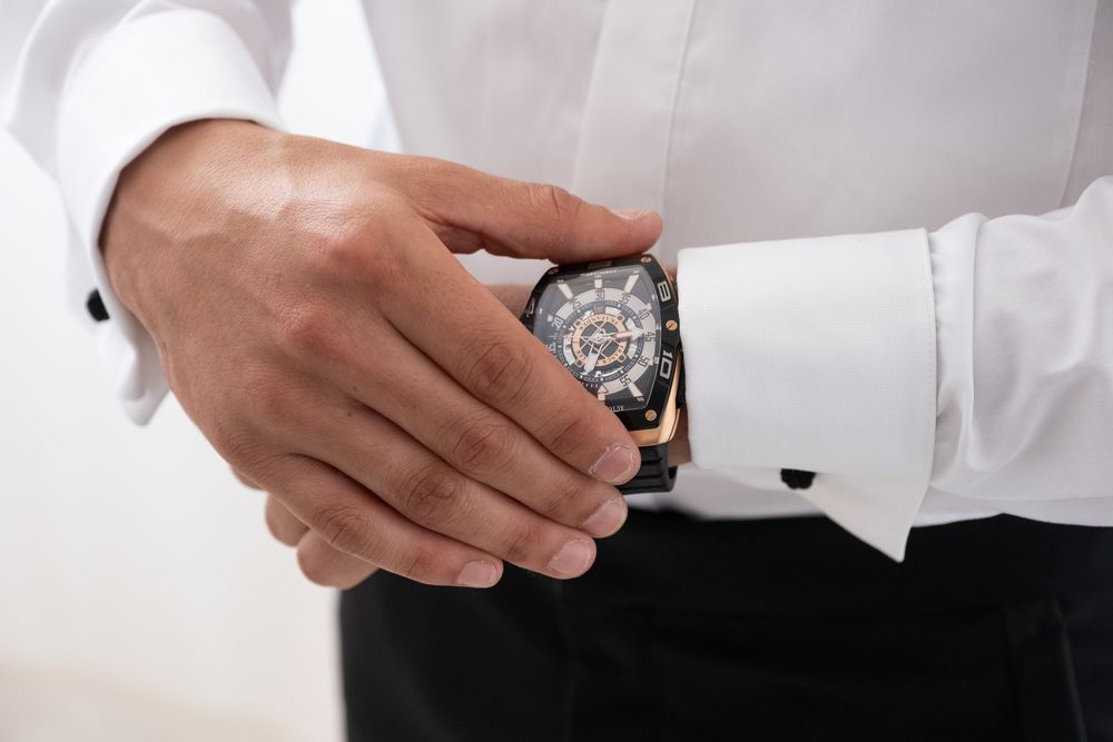 Close-up of hands adjusting luxurious watch with white shirt cuff.