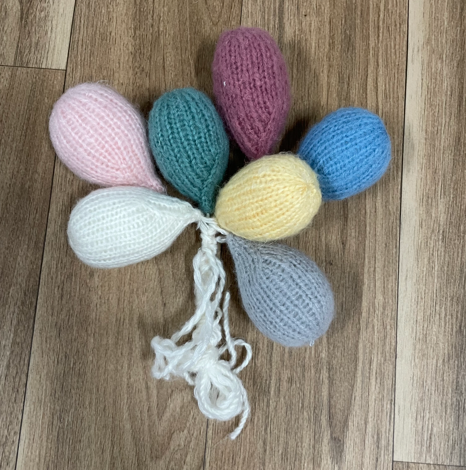A collection of colorful knitted balloon-shaped ornaments tied together on wooden flooring.