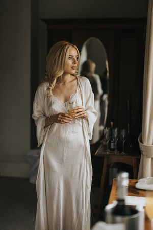 A bride stands thoughtfully by a mirror in a softly lit interior setting at Cleatham Hall.