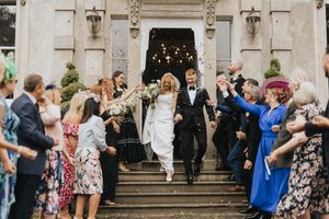 Wedding guests throw confetti at newlyweds on ornate stone steps of Cleatham Hall.