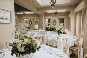 An elegant wedding reception room at Cleatham Hall with round tables decorated in white floral centrepieces and natural lighting.