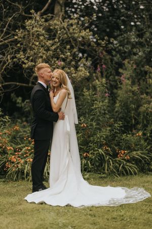 A romantic garden wedding scene shows a couple sharing intimate moments among blooming flowers at Cleatham Hall.