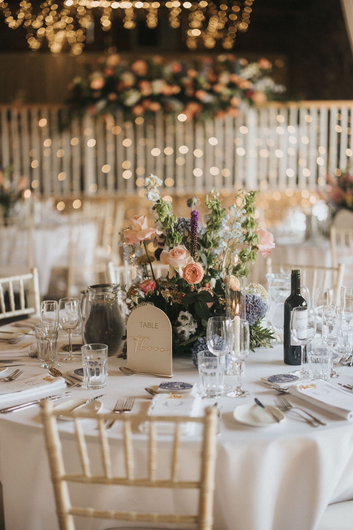 Elegant white bridal shoes and accessories including pearl necklace and rings arranged on a dark wooden surface.