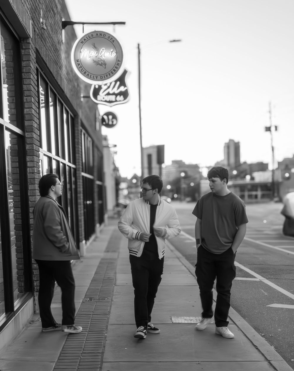 Three people engaged in conversation while standing on a sidewalk outside a brick building with a vintage clock sign.