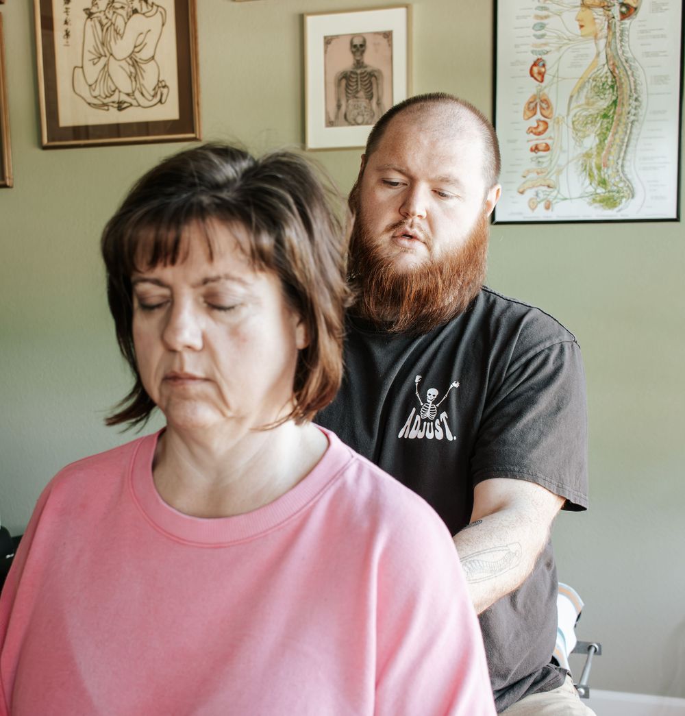 A chiropractor performs therapeutic work on a patient in pink while anatomical charts hang on the wall.