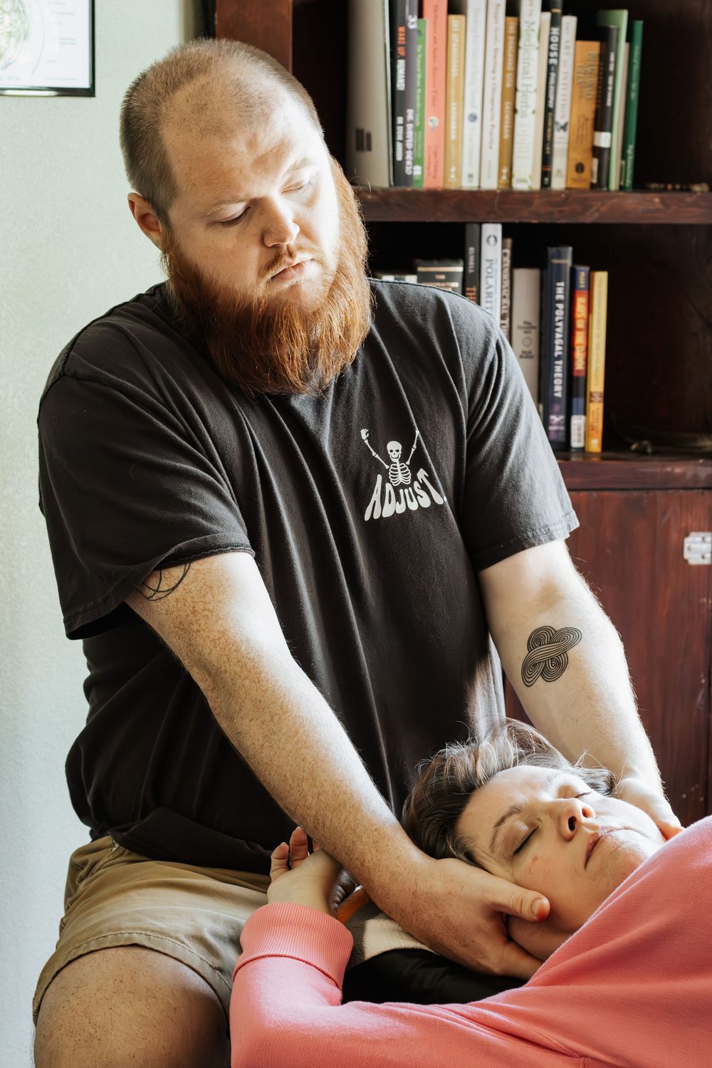 A chiropractor wearing a black t-shirt performs neck manipulation on a client lying on a treatment table.