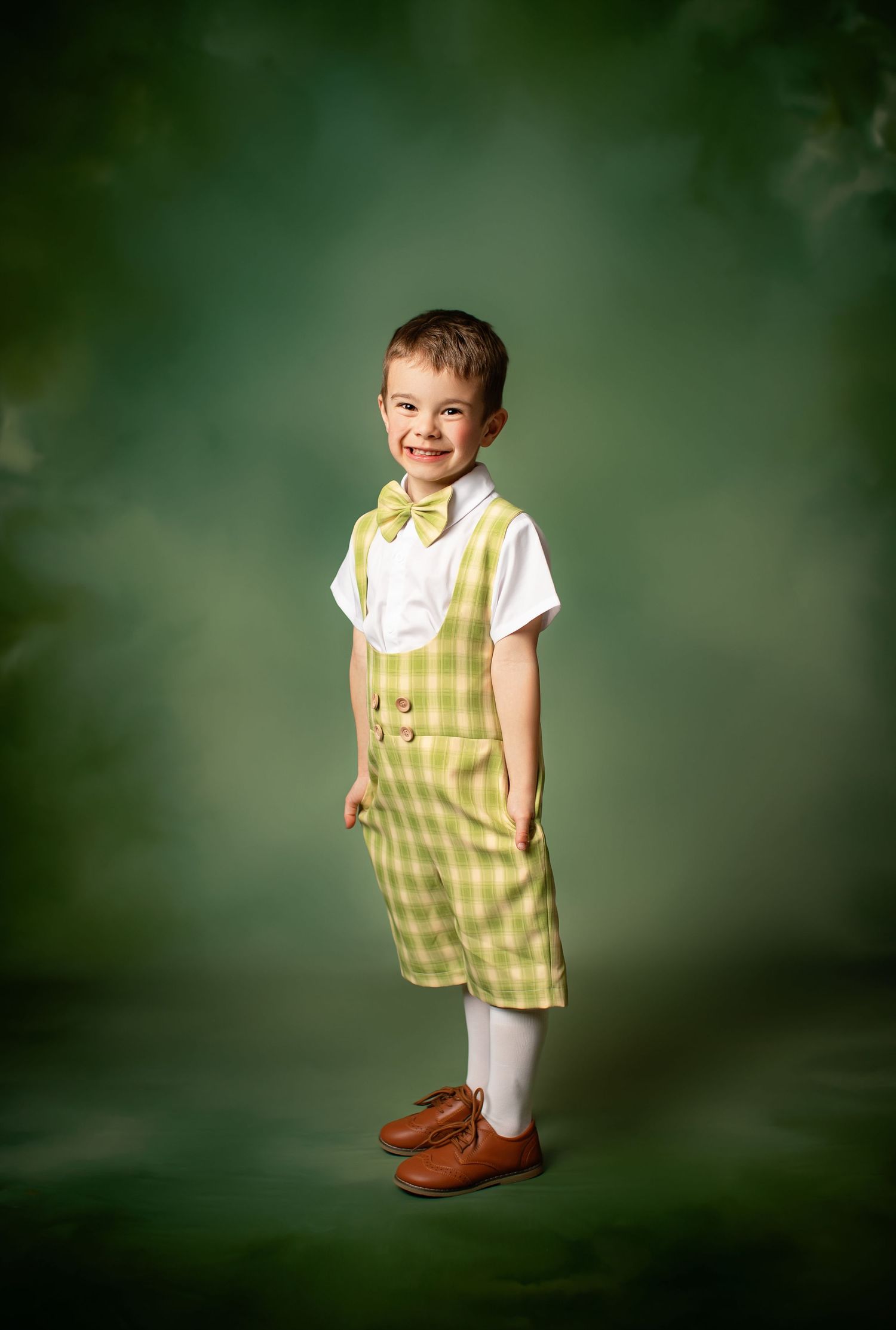 Vintage-styled portrait against a green backdrop showing a child in yellow plaid shorts, white shirt and yellow bow tie.