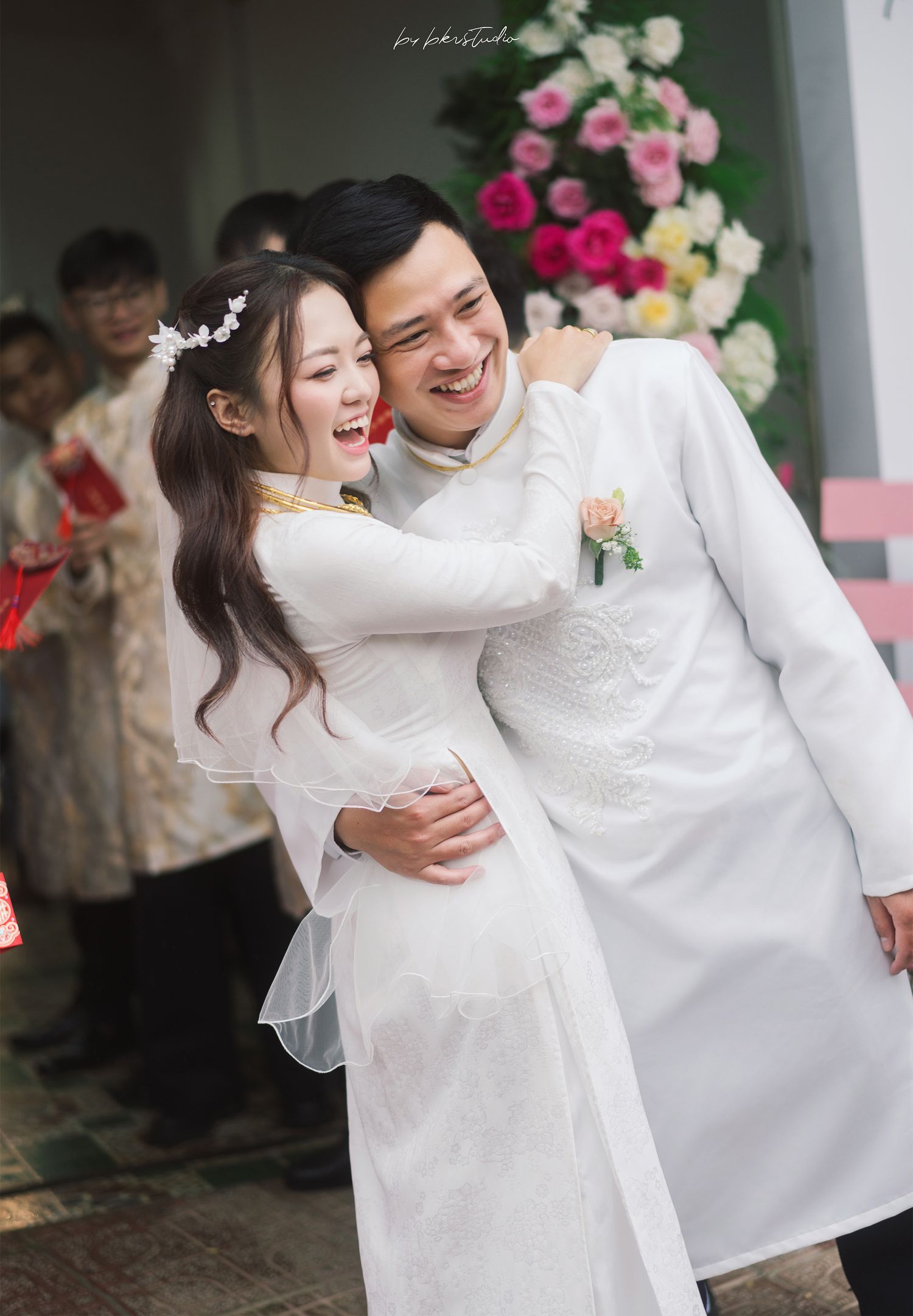 A joyful couple in traditional white ao dai outfits share an intimate moment at their wedding ceremony.