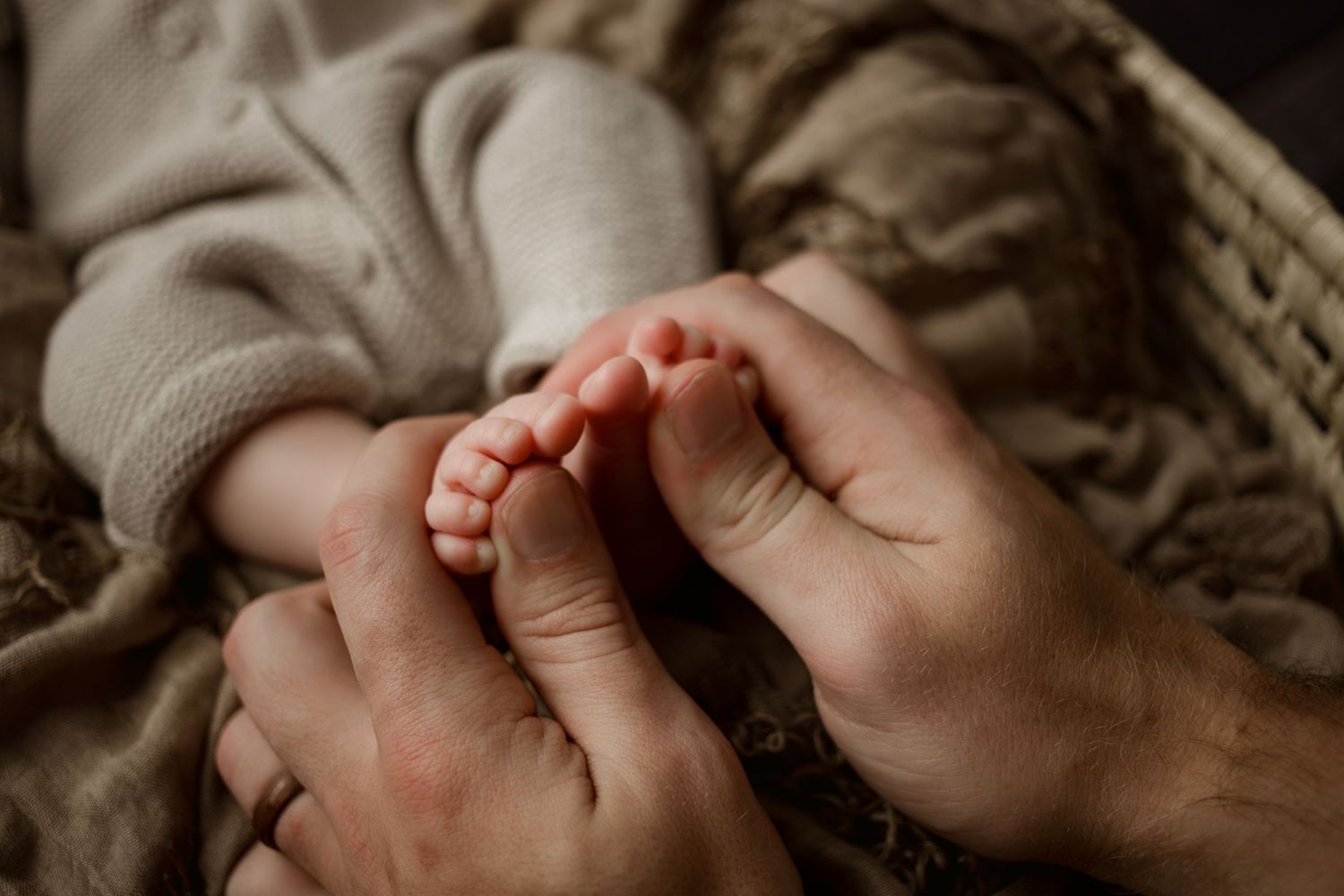A close up shot of small baby feet being gently held in adult hands on a soft blanket.