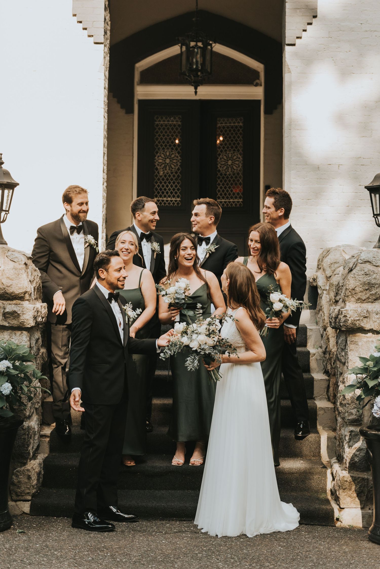 Wedding party gathers on stone steps of historic building entrance in warm moody lighting.