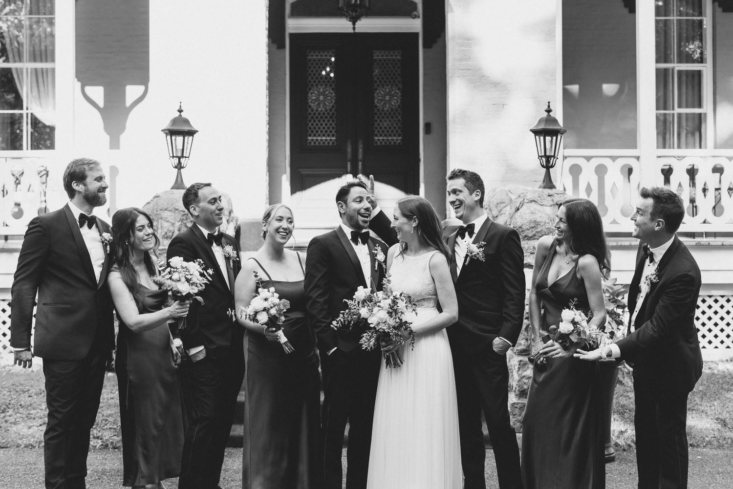 Wedding party gathered casually outside luxury house entrance with lanterns in black and white photograph.