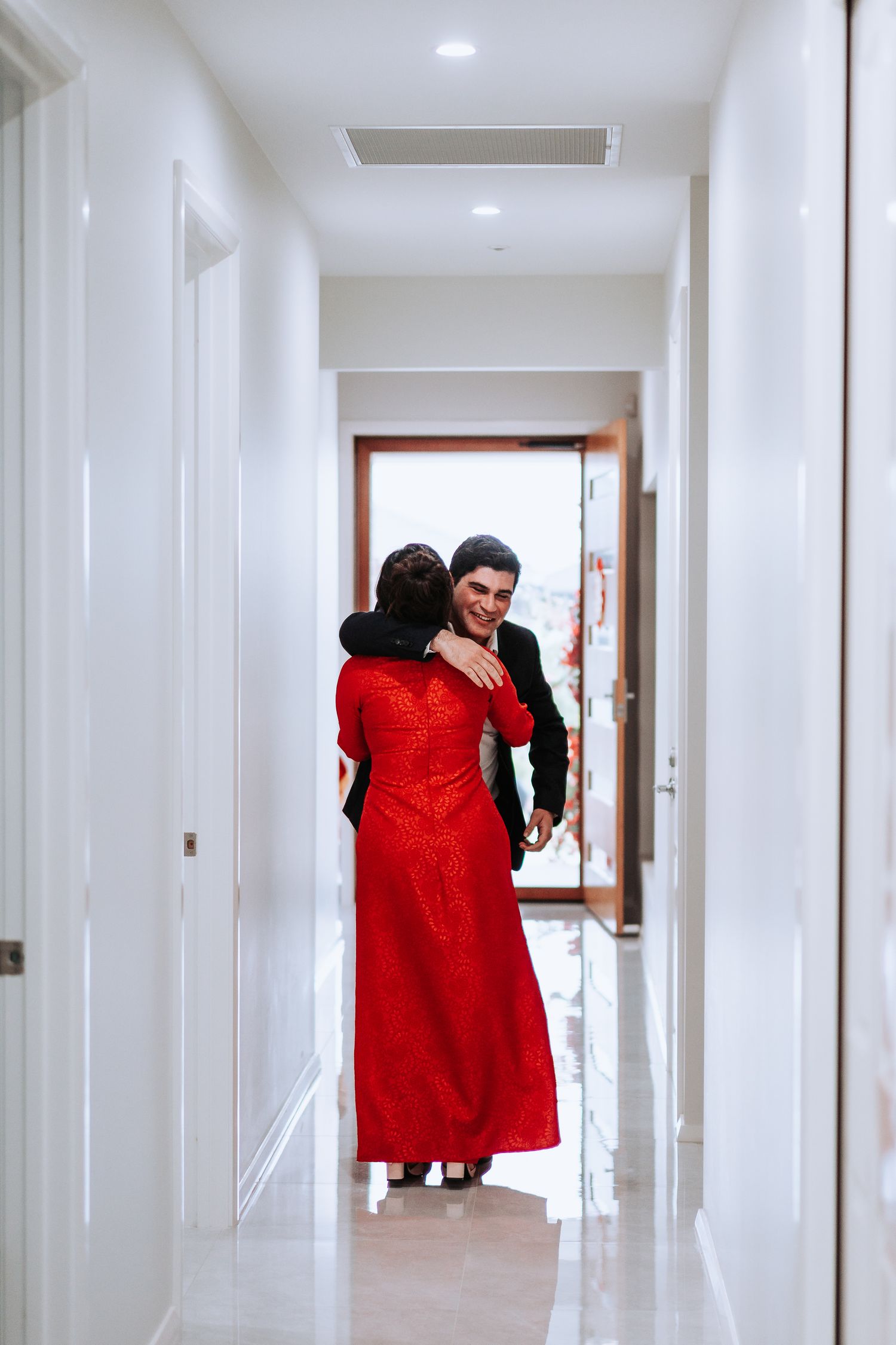 A tender moment captured between a couple in red attire in a bright white hallway.