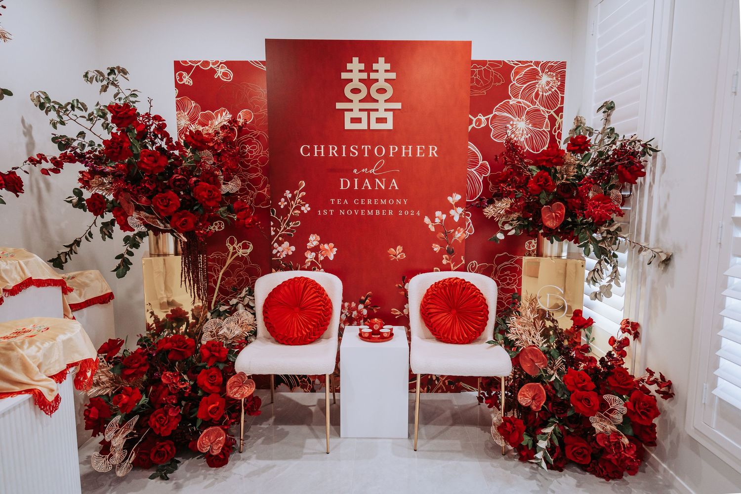Traditional Chinese wedding decoration with double happiness symbol, white chairs and red floral arrangements.