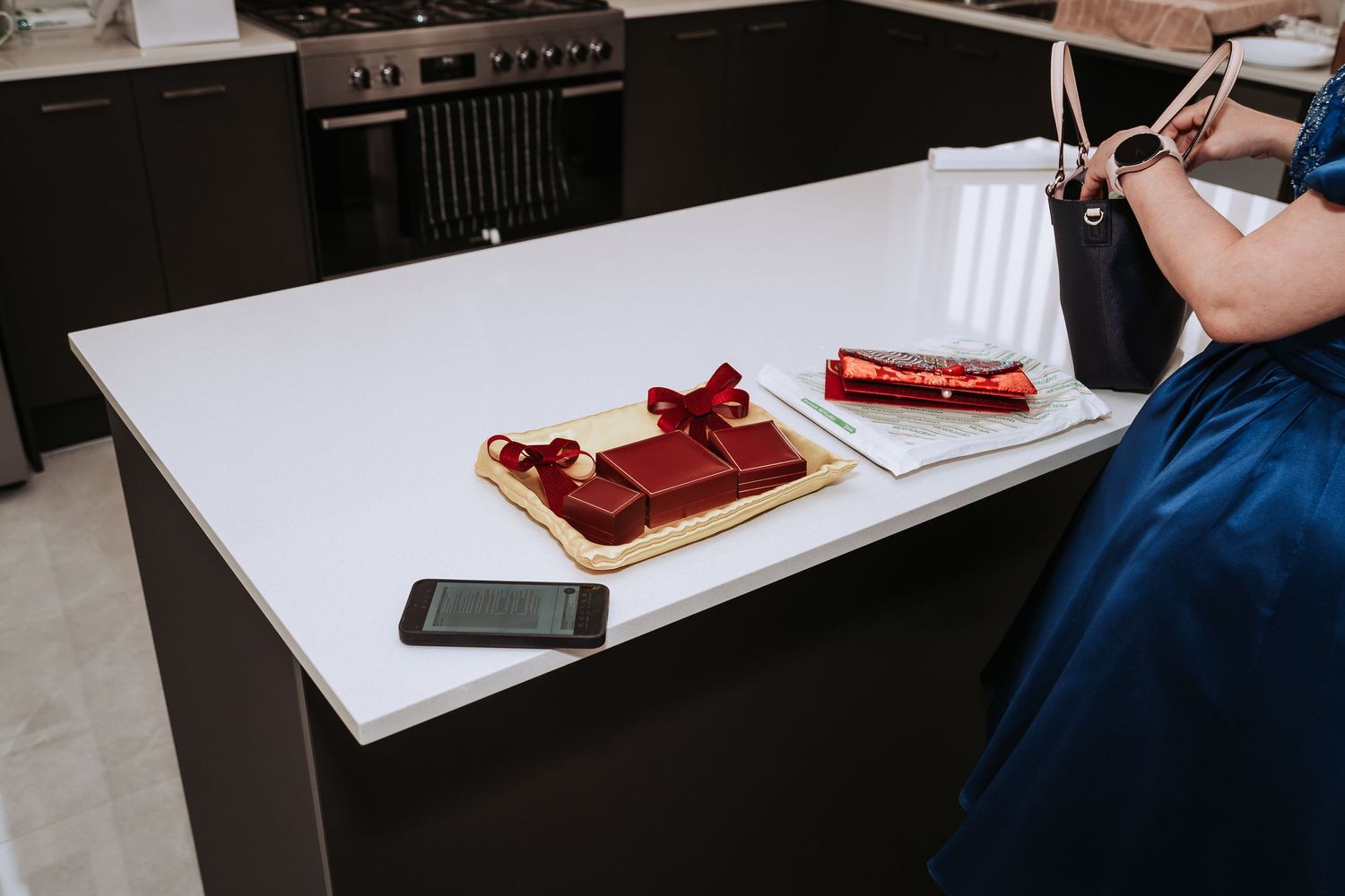 Someone makes a peanut butter and jelly sandwich on white bread at a kitchen counter with a phone nearby.