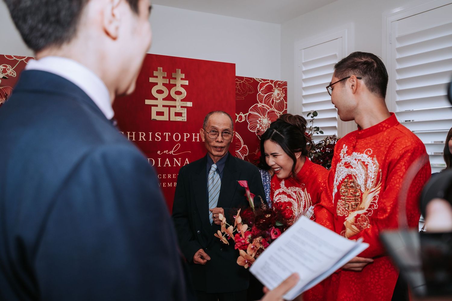 Traditional Chinese wedding ceremony with double happiness symbol backdrop and participants in red traditional attire.