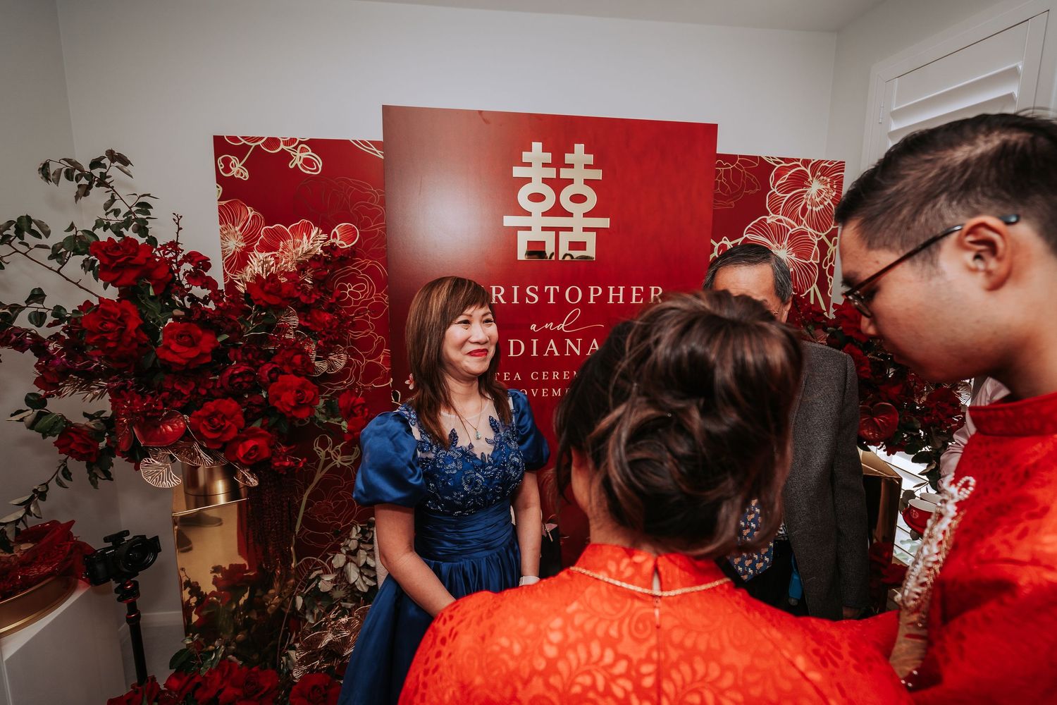 Wedding celebration with traditional double happiness symbol and red floral decorations in the background.