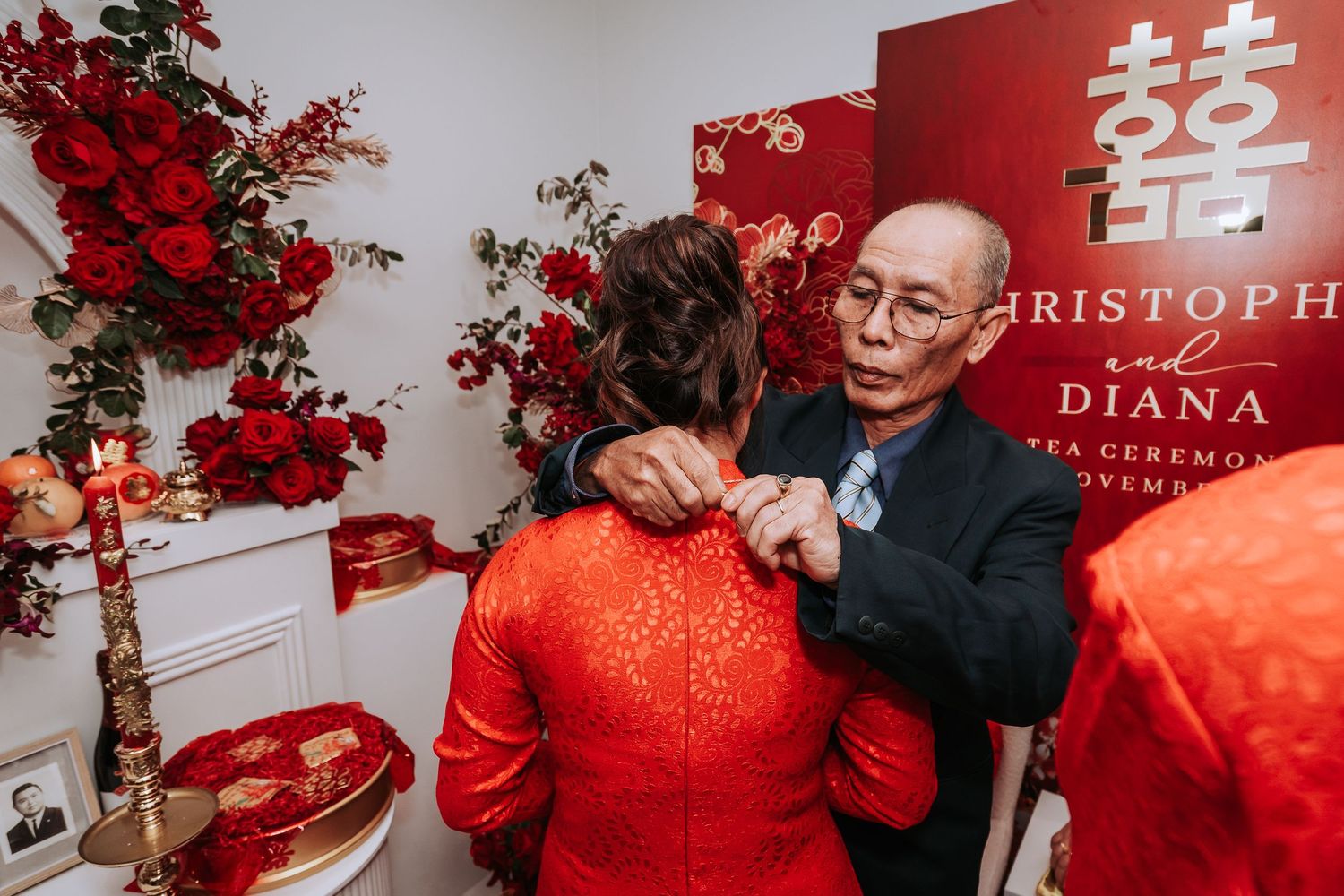 Traditional Chinese wedding scene with embracing couple in red qipao dress and black suit against red double happiness backdrop.