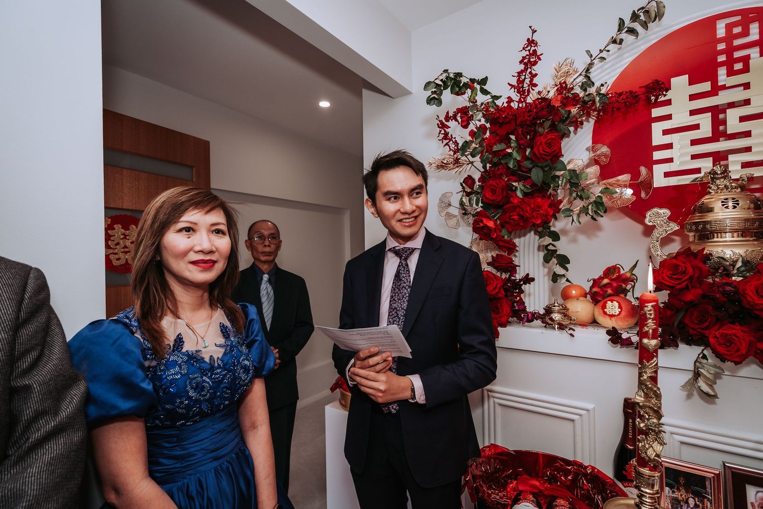 People gather at a festive Chinese New Year celebration with red decorations and floral arrangements.