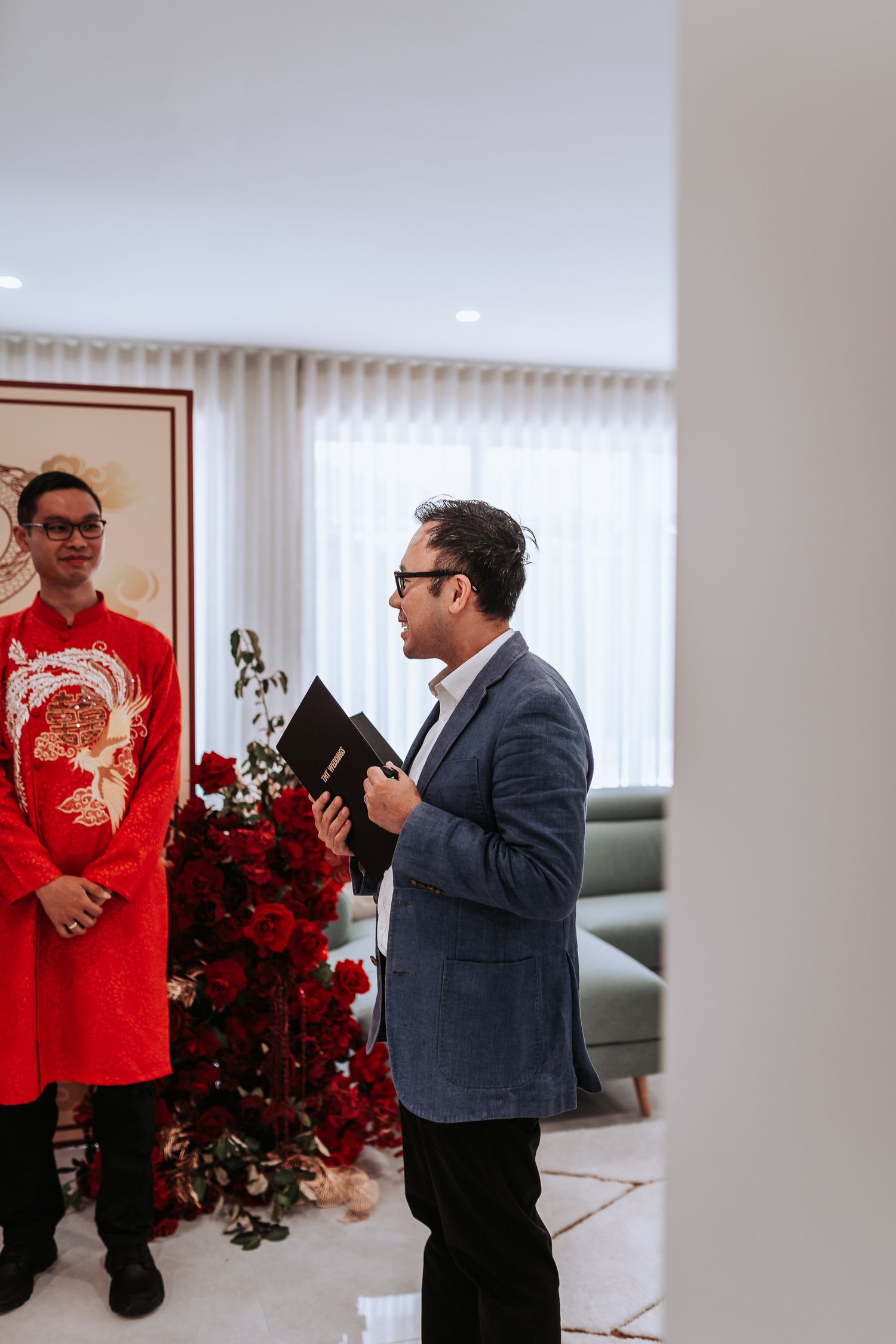 A ceremony taking place with red floral arrangements and someone in formal attire holding documents.