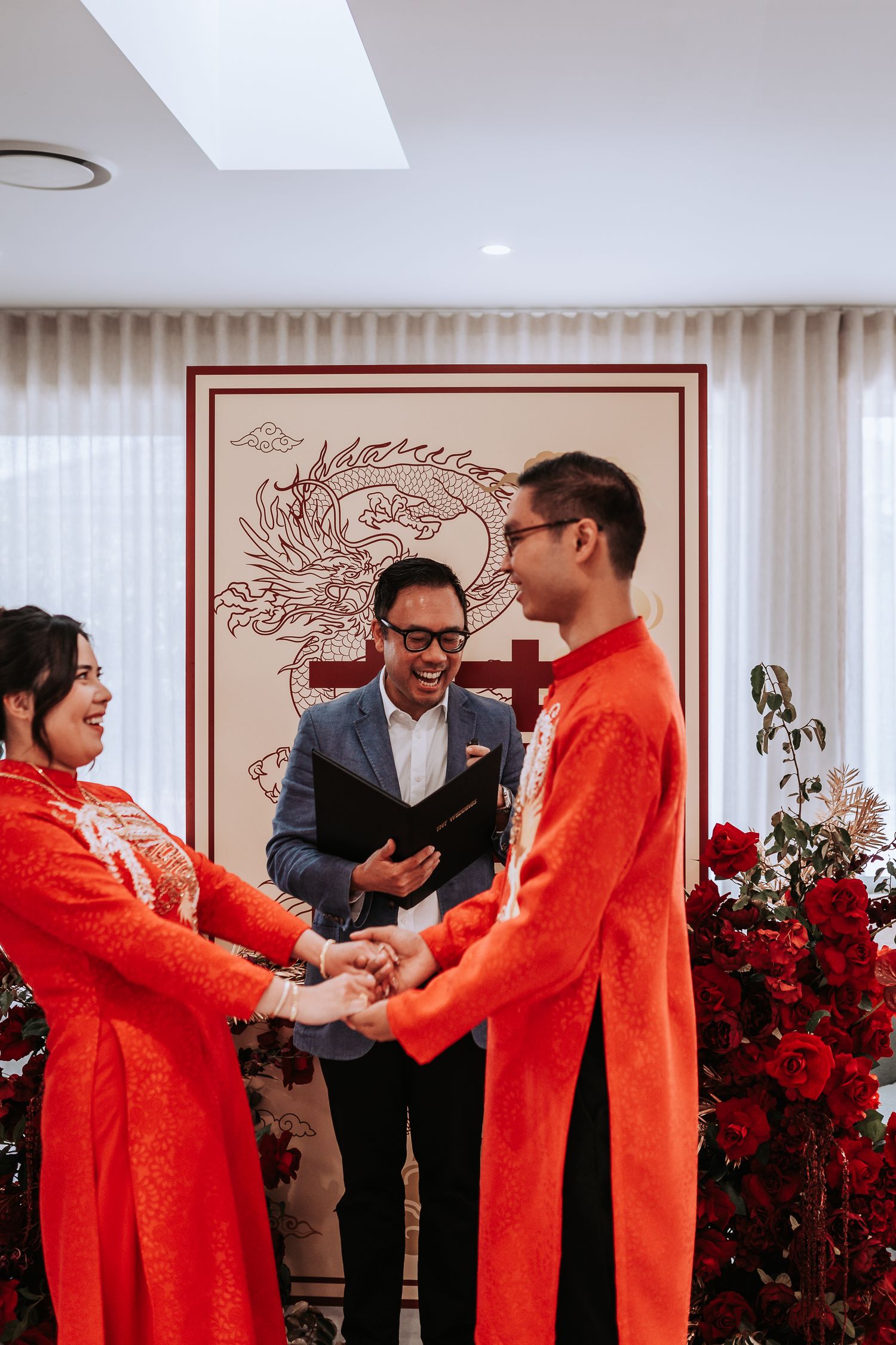 Traditional Chinese wedding ceremony with a couple in red outfits and an officiant in front of a dragon backdrop.