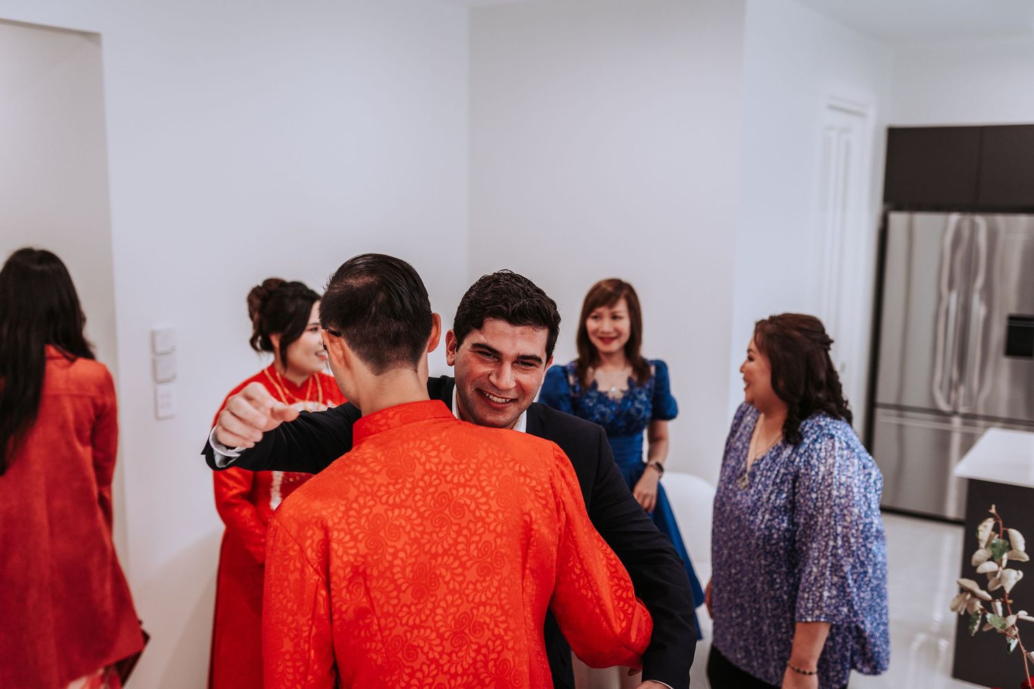A group of people gathered in a white room, with several wearing bright orange clothing during a social gathering.