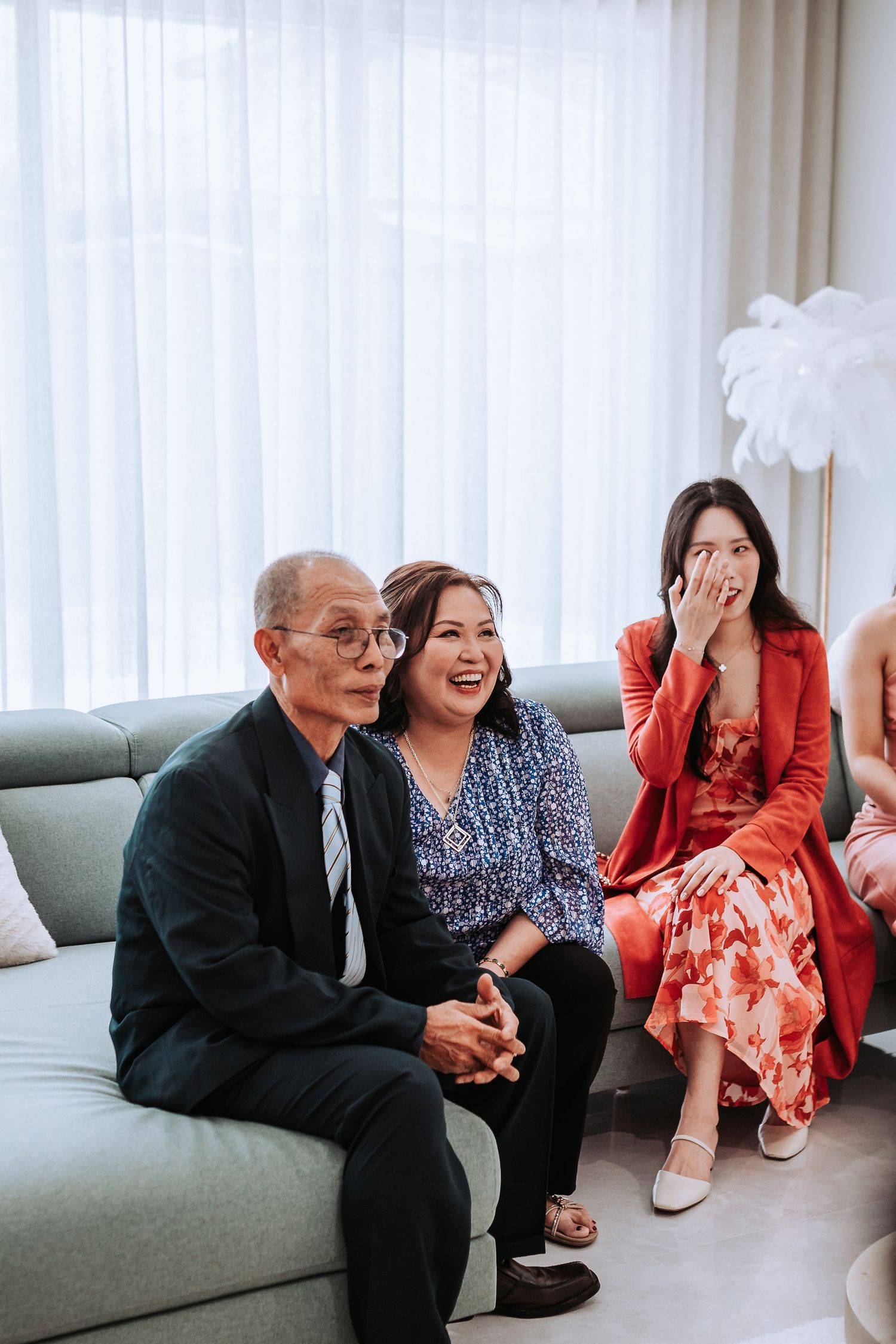 A group of people sitting together on a gray couch, sharing a joyful moment and laughing in a bright living room.