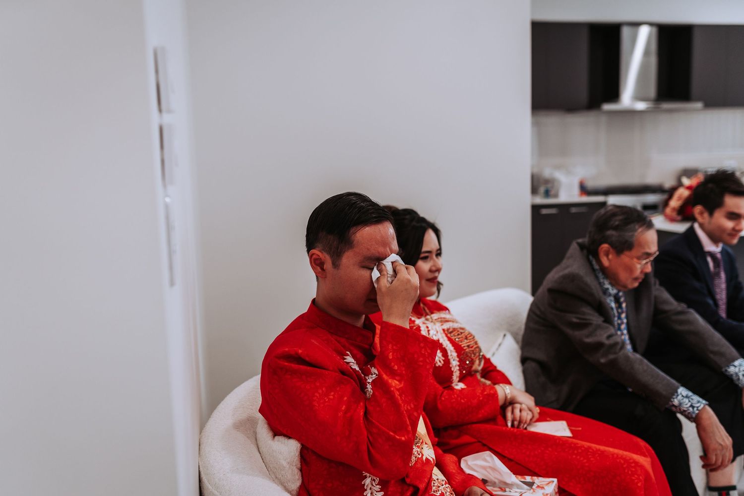 Wedding guests in red traditional Chinese attire seated indoors during celebration ceremony.