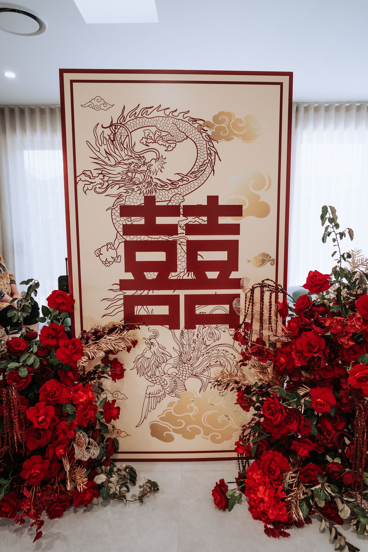 Traditional Chinese wedding backdrop with double happiness symbol and dragon design surrounded by red roses decoration.
