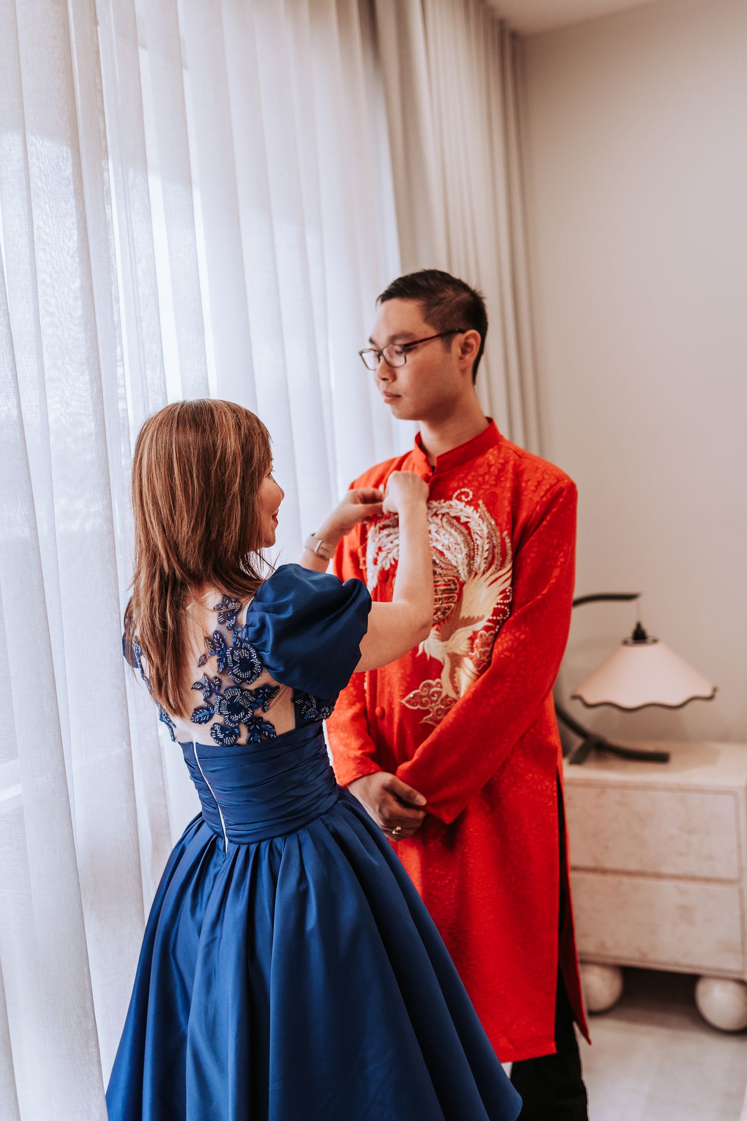 A couple in traditional wedding attire, with the bride in blue and groom in red, share an intimate moment.