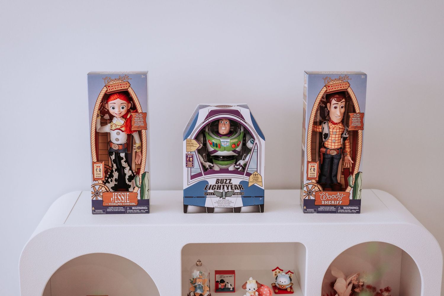 Three Toy Story character dolls displayed in boxes on a white shelf including Buzz Lightyear and Jessie.