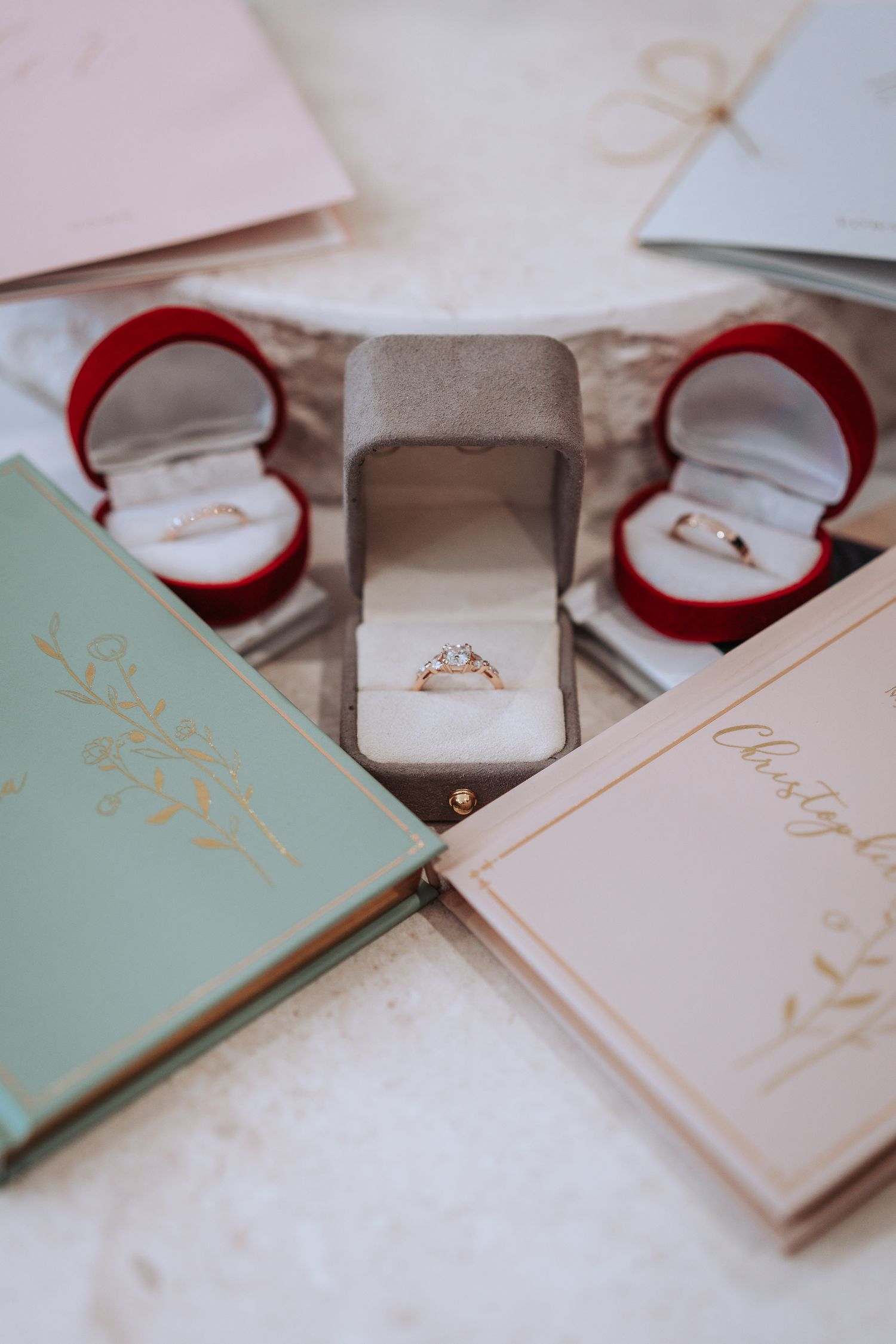 Elegant engagement rings in red velvet boxes displayed with mint green and blush pink wedding planning books.