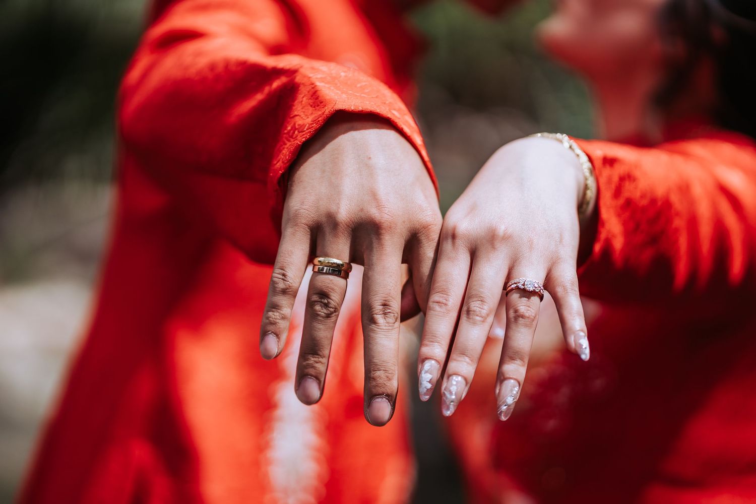 Close-up of hands wearing engagement rings against backdrop of red traditional clothing.