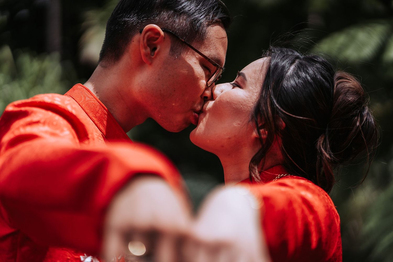 Romantic couple in matching red traditional outfits sharing an intimate moment in a garden setting.