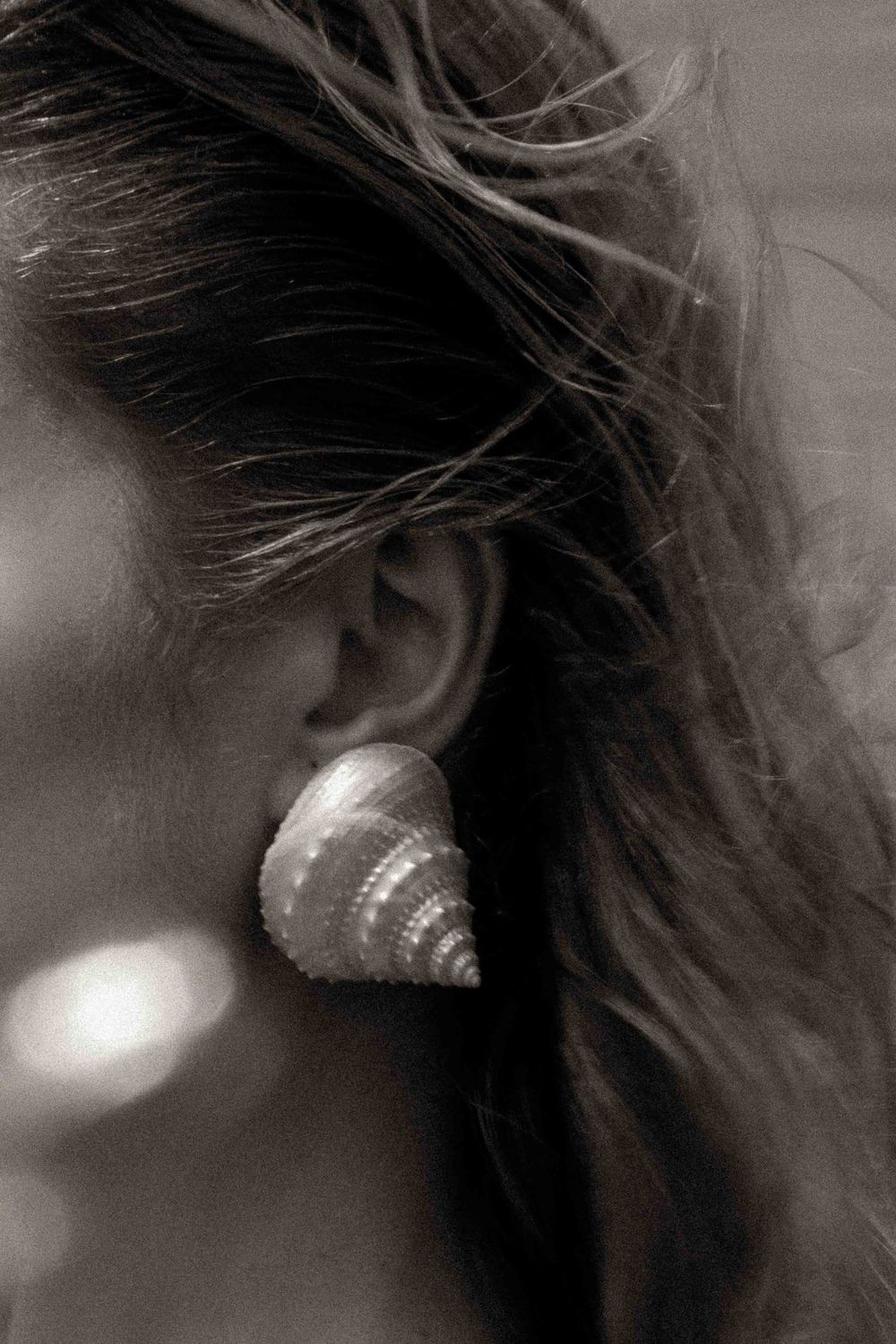 Seashell earring detail against flowing hair in black and white.