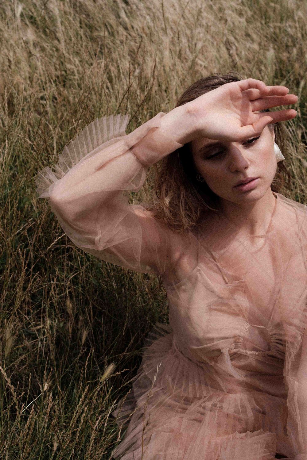 Dreamy portrait in sheer tulle dress against field of wild grass.