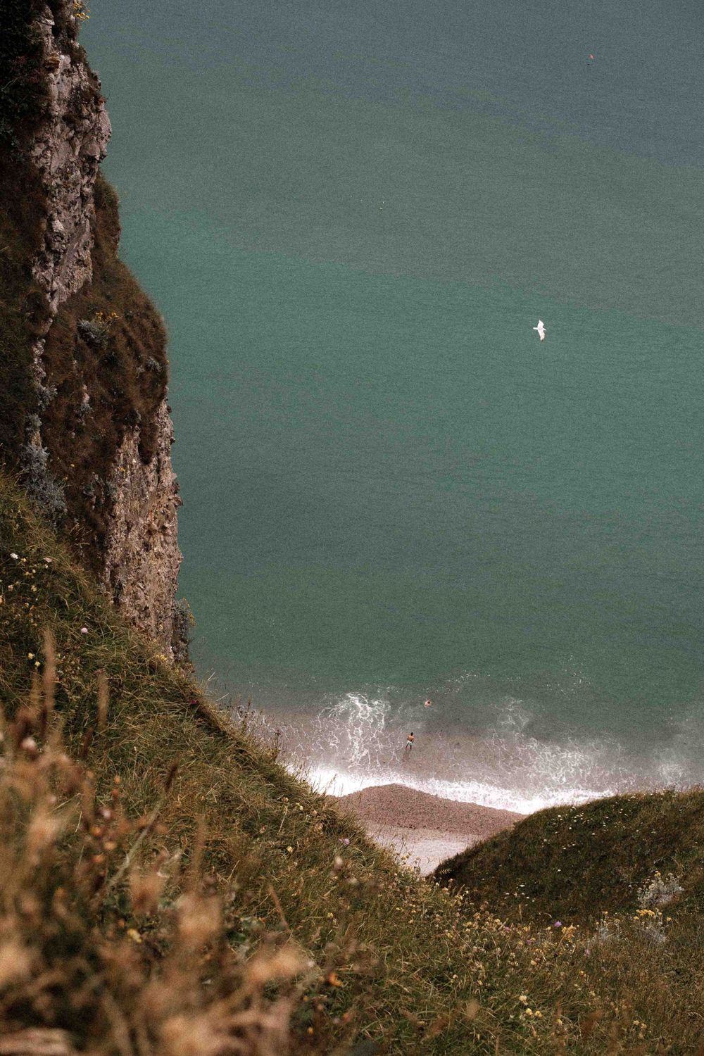 Dramatic coastal cliff overlooks turquoise waters with white waves crashing below.