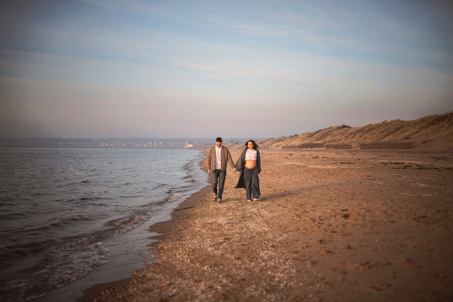 Couple walking together along a serene beach at sunset.